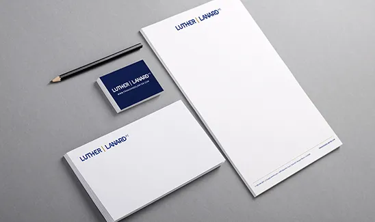 A set of stationery items including a letterhead, business cards, and a pencil on a gray surface. The letterhead and business cards display the "Luther Laward" branding in blue text.