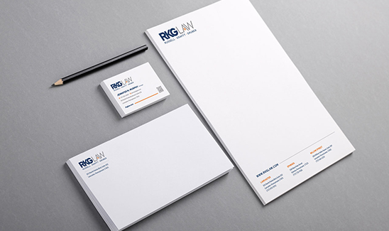 A flat lay image showing branded RKG Law stationery including a letterhead, business card, envelope, and pencil on a gray background.