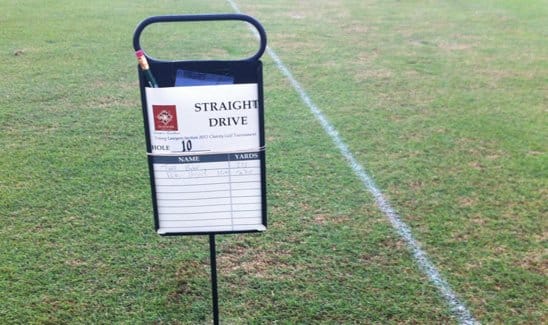 A sign on a grassy field reads "Straight Drive" for Hole 10. It features a scorecard with columns for names and yards, and a slot holding a pencil.