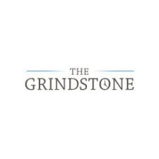 The image shows the logo for "The Grindstone," featuring the website name with a clock symbol replacing the letter "O" in "Grindstone." The logo has a minimalist design with blue lines.