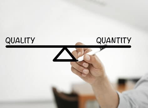 A hand is drawing a balanced scale with the words "Quality" on the left side and "Quantity" on the right side, indicating an equilibrium.