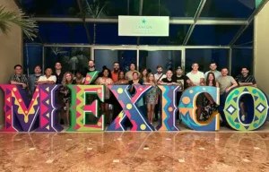 Group of people standing behind large colorful "MÉXICO" letters inside a building.
