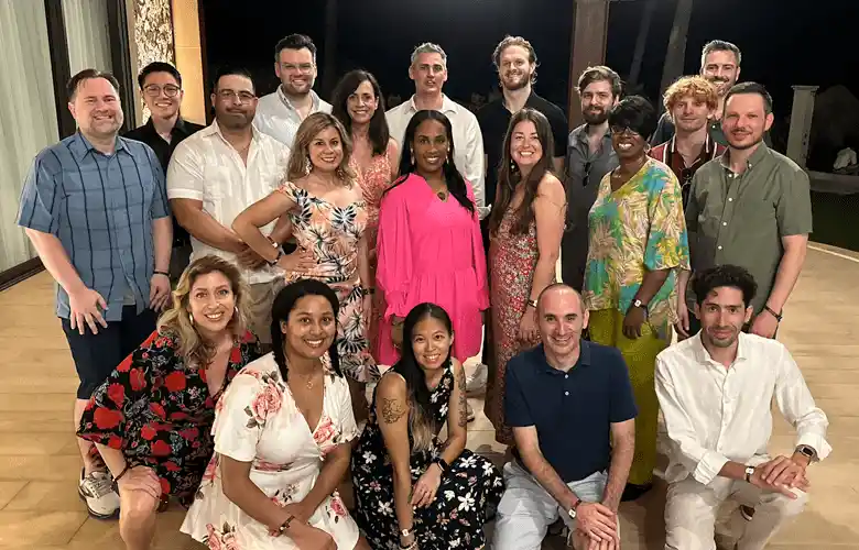 A group of twenty people pose together indoors, smiling for a group photo.