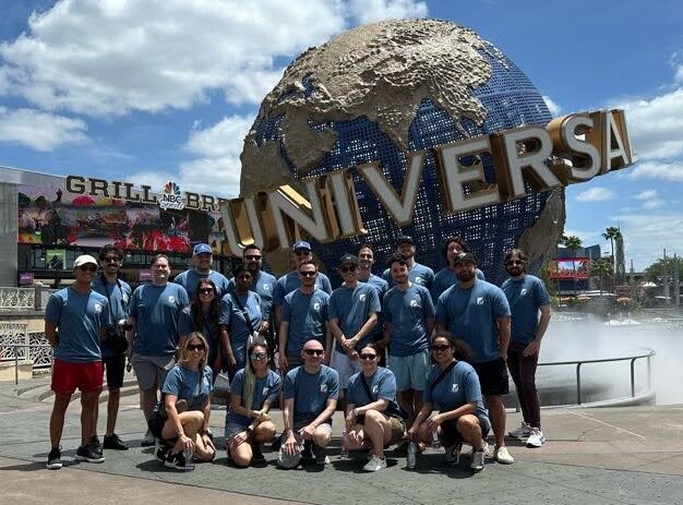 Group of people in blue shirts posing in front of the Universal Studios globe landmark.