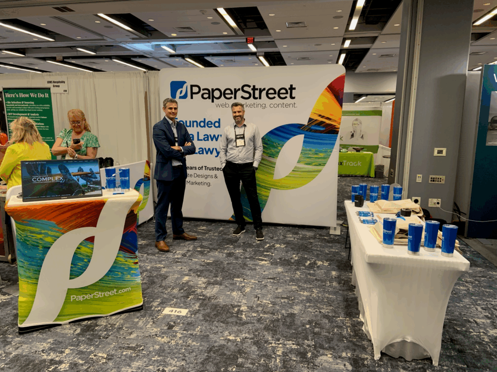 Two people stand at a PaperStreet booth at a conference, with branded items on display.