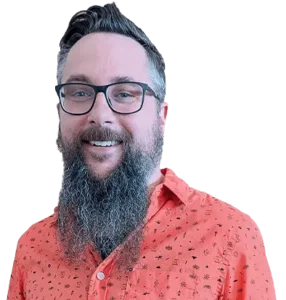 Man with glasses and a long beard wearing an orange patterned shirt, smiling at the camera.